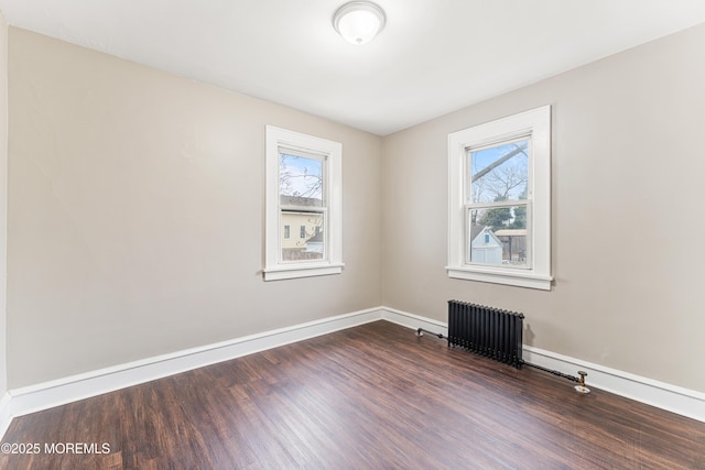 spare room with radiator heating unit, baseboards, and wood finished floors