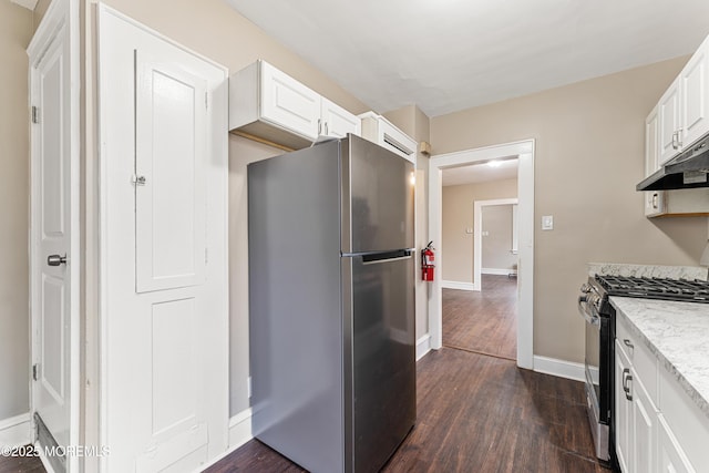 kitchen with light stone counters, under cabinet range hood, dark wood-style flooring, range with gas stovetop, and freestanding refrigerator