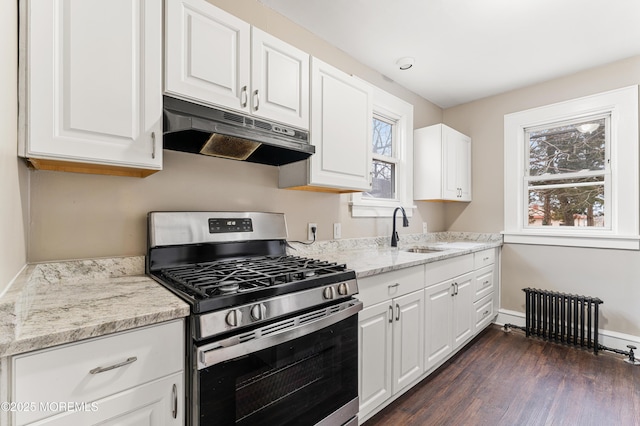 kitchen featuring radiator heating unit, a sink, under cabinet range hood, a wealth of natural light, and gas stove