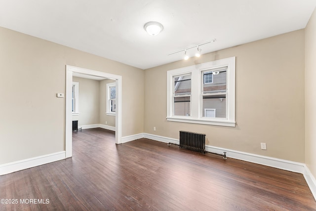 spare room featuring radiator heating unit, dark wood finished floors, and baseboards