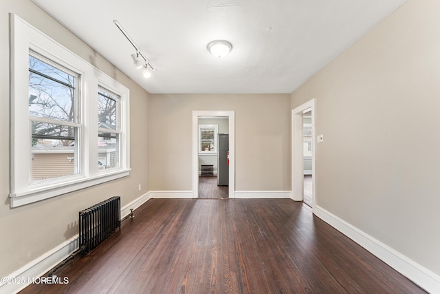 unfurnished room featuring track lighting, radiator, dark wood finished floors, and baseboards