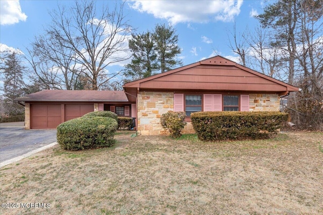 view of front of house featuring driveway, stone siding, a garage, and a front yard