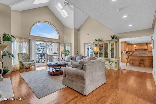 living room with a textured ceiling, high vaulted ceiling, a skylight, visible vents, and light wood finished floors