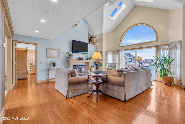 living room with a skylight, a glass covered fireplace, light wood-style flooring, and baseboards