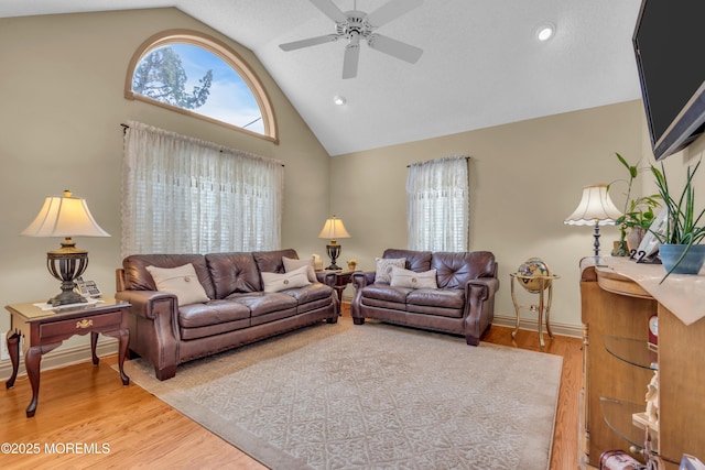 living area with high vaulted ceiling, light wood-type flooring, a ceiling fan, and baseboards