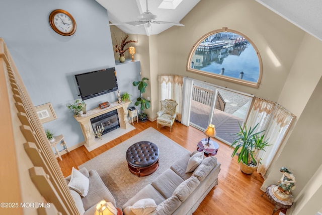 living room featuring ceiling fan, high vaulted ceiling, a skylight, a fireplace, and wood finished floors