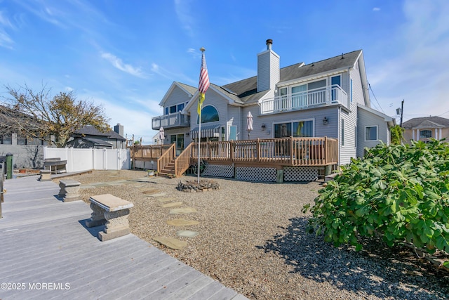 back of property featuring a balcony, a chimney, fence, and a deck