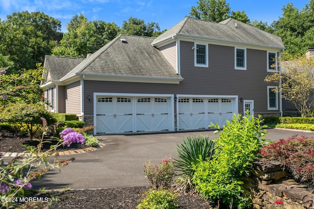 view of side of home with a garage, driveway, a shingled roof, and stone siding