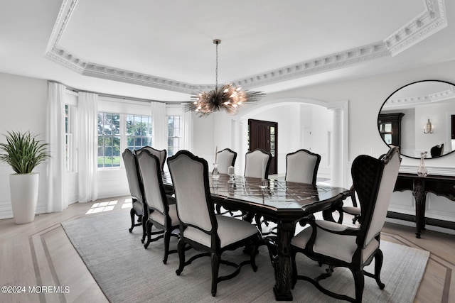 dining space featuring arched walkways, decorative columns, a raised ceiling, an inviting chandelier, and ornamental molding