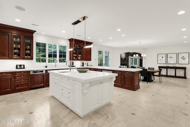 kitchen with a kitchen island with sink, a peninsula, visible vents, light countertops, and glass insert cabinets