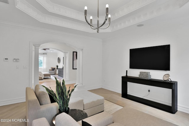 living area with a tray ceiling, arched walkways, crown molding, an inviting chandelier, and ornate columns