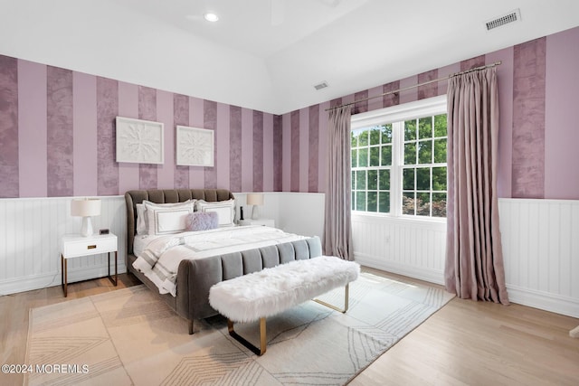 bedroom featuring lofted ceiling, wood finished floors, wainscoting, and wallpapered walls