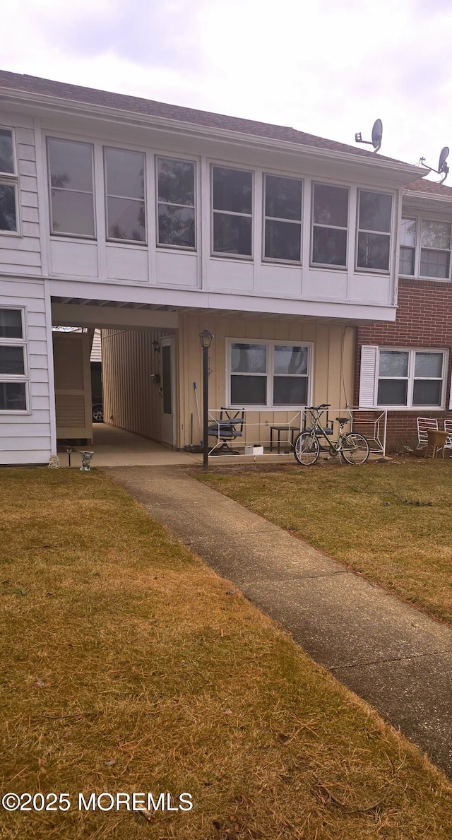 back of property featuring a yard, aphalt driveway, board and batten siding, and brick siding