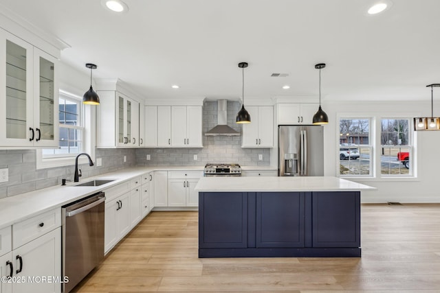 kitchen featuring a sink, a kitchen island, white cabinets, wall chimney range hood, and appliances with stainless steel finishes