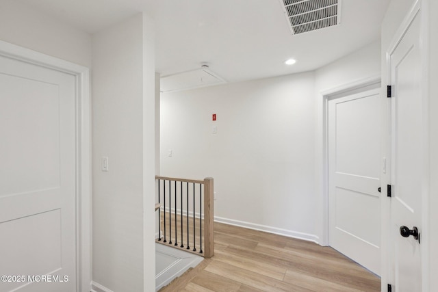 corridor with attic access, visible vents, baseboards, an upstairs landing, and light wood-style floors