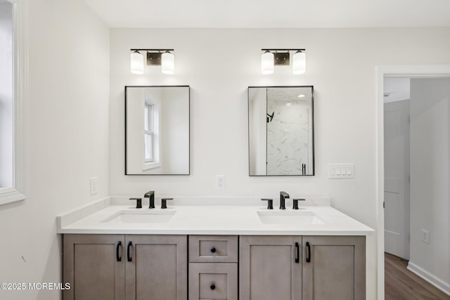 full bath with double vanity, walk in shower, a sink, and wood finished floors