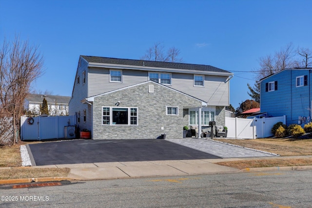 view of front of property featuring driveway, stone siding, and a gate