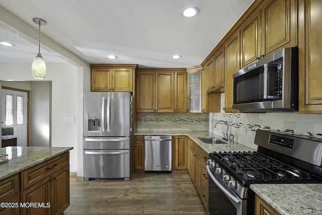 kitchen featuring brown cabinetry, light stone counters, stainless steel appliances, and a sink