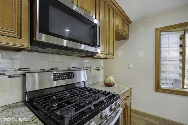 kitchen featuring light stone counters, dark wood-style flooring, stainless steel appliances, decorative backsplash, and brown cabinetry