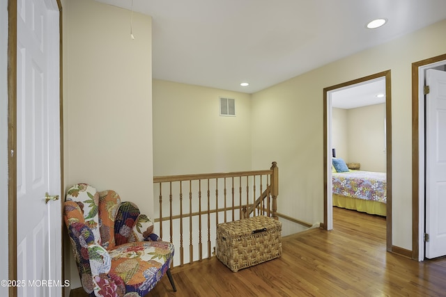 hall featuring an upstairs landing, wood finished floors, visible vents, and recessed lighting