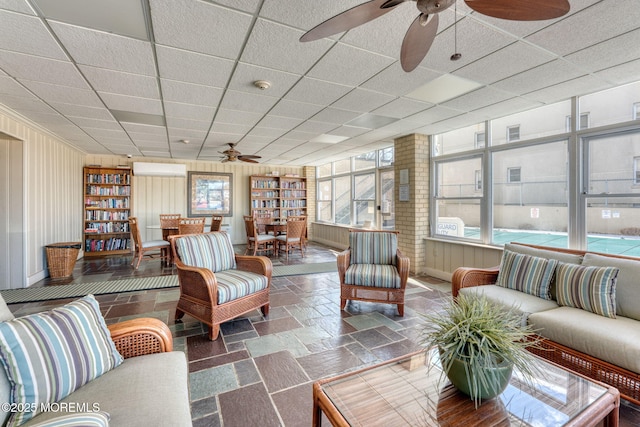 living area featuring a paneled ceiling, ceiling fan, wooden walls, and stone tile flooring