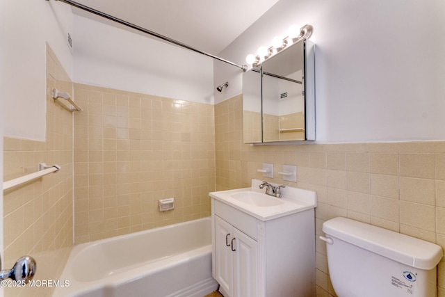 full bathroom featuring shower / washtub combination, a wainscoted wall, tile walls, toilet, and vanity