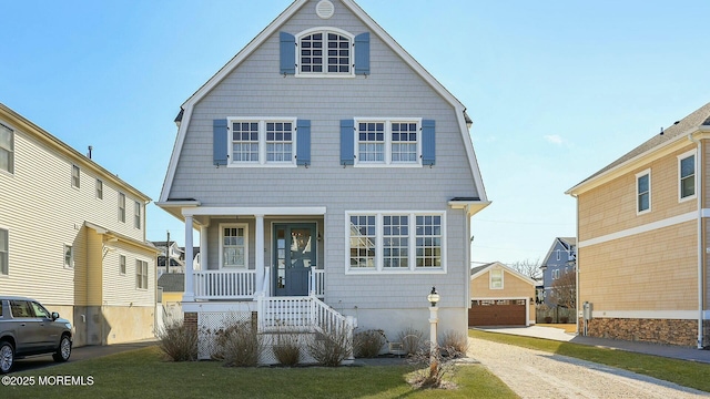 view of front of home with an outbuilding, a porch, a detached garage, and a gambrel roof