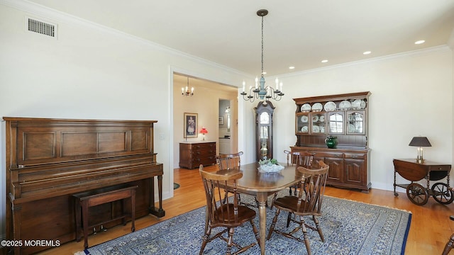 dining room featuring an inviting chandelier, light wood-type flooring, visible vents, and crown molding