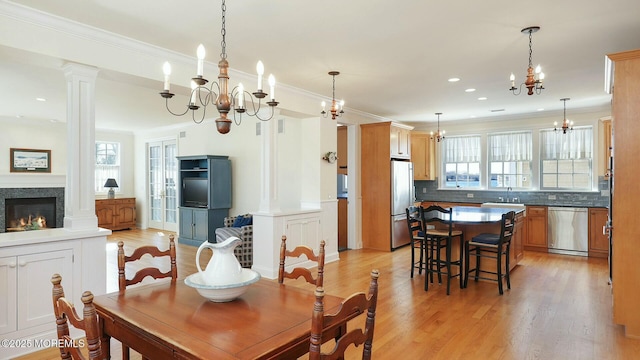 dining space with light wood-type flooring, decorative columns, crown molding, and a glass covered fireplace