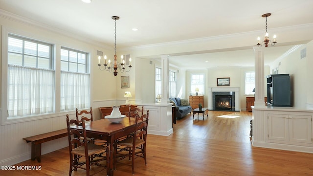 dining area featuring light wood finished floors, decorative columns, visible vents, a glass covered fireplace, and crown molding