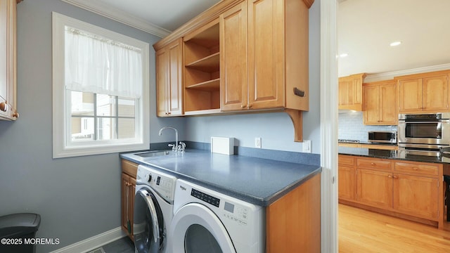 clothes washing area featuring cabinet space, light wood finished floors, washer and clothes dryer, ornamental molding, and a sink