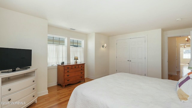 bedroom with light wood finished floors, baseboards, visible vents, an inviting chandelier, and a closet