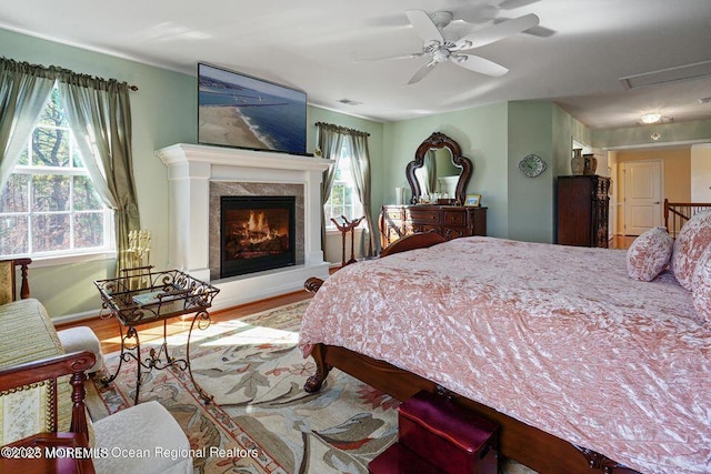 bedroom with visible vents, a ceiling fan, a high end fireplace, wood finished floors, and baseboards