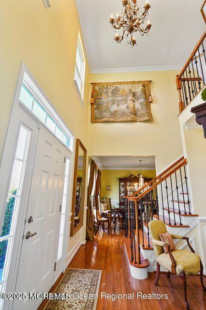 entryway with crown molding, wood finished floors, and a notable chandelier