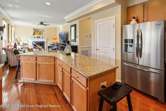 kitchen with a warm lit fireplace, dark wood-style floors, open floor plan, crown molding, and stainless steel refrigerator with ice dispenser