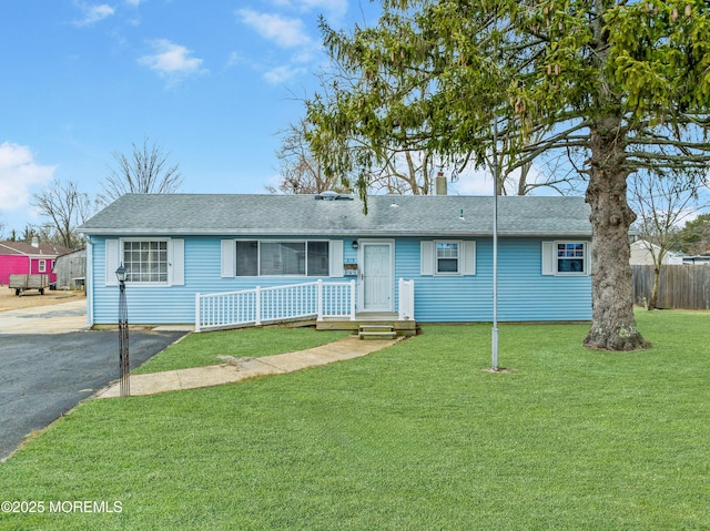 ranch-style home featuring a front lawn, a shingled roof, fence, and aphalt driveway