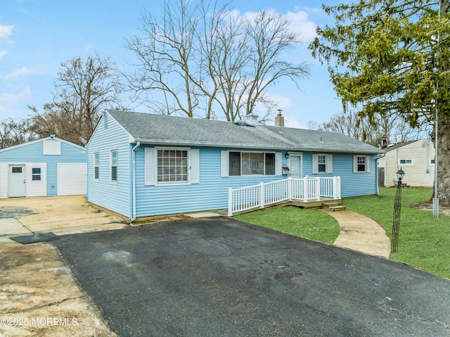 ranch-style house featuring a detached garage, a chimney, aphalt driveway, roof with shingles, and a front yard