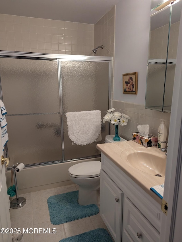 bathroom with shower / bath combination with glass door, tile walls, toilet, vanity, and tile patterned flooring