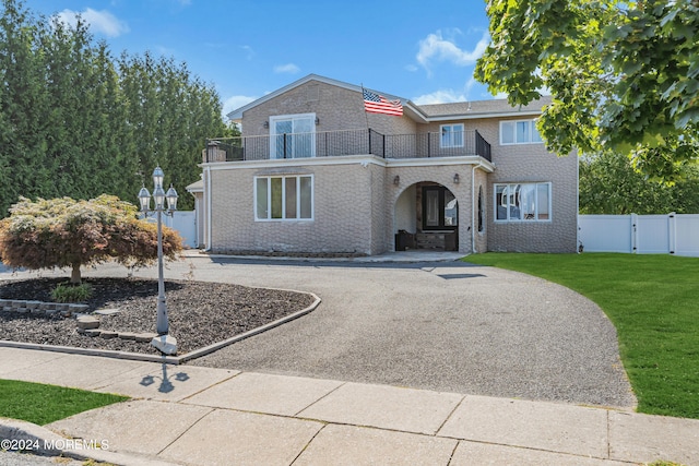 view of front of property with driveway, a balcony, a gate, fence, and a front lawn