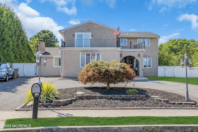 traditional-style home featuring a balcony, a gate, fence, and aphalt driveway