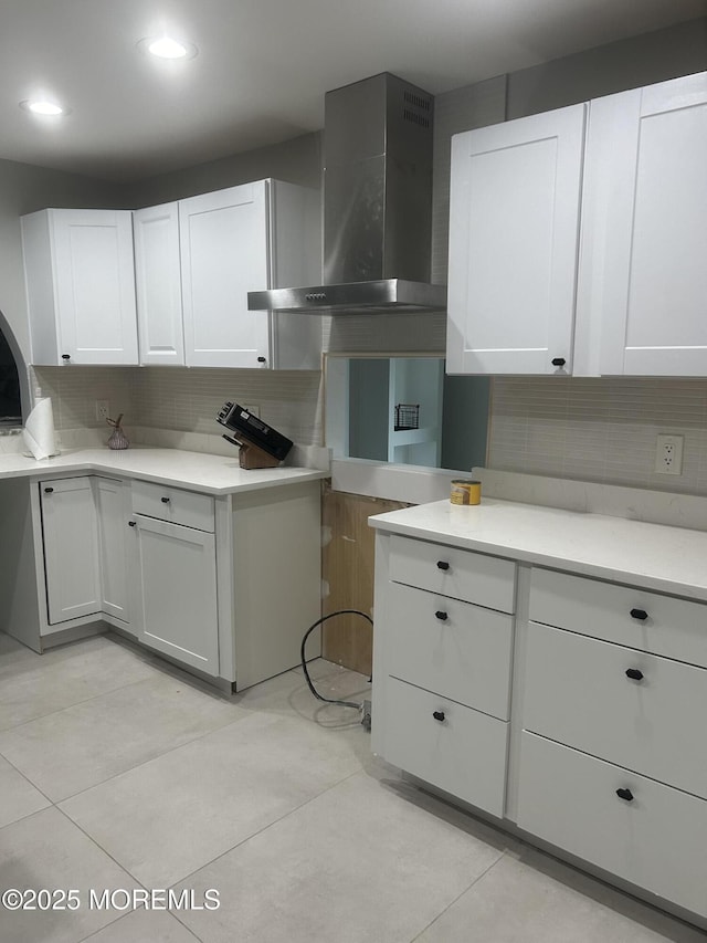 kitchen featuring wall chimney exhaust hood, white cabinets, backsplash, and light countertops