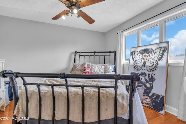 bedroom featuring light wood-style flooring, baseboards, ceiling fan, and a textured ceiling