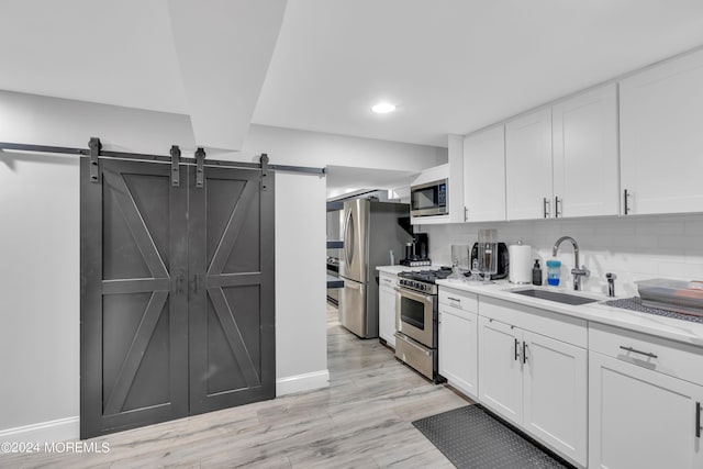 kitchen with stainless steel appliances, a barn door, a sink, and white cabinets