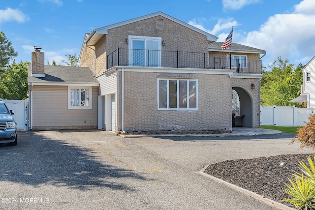 view of front of property with a balcony, a garage, fence, driveway, and a gate