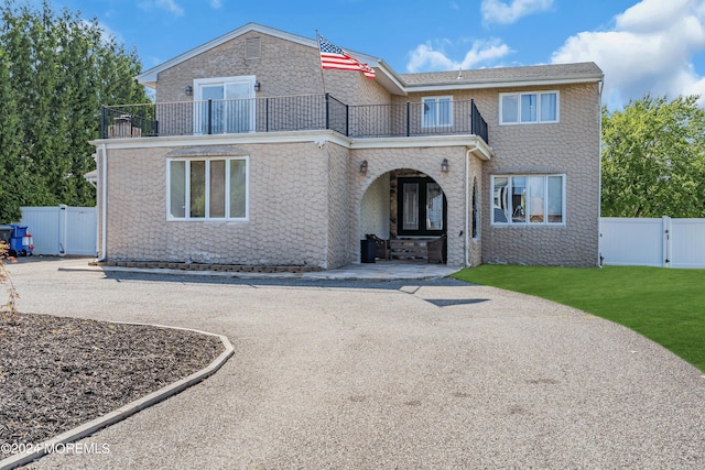 view of front facade featuring a balcony, a gate, fence, and a front yard