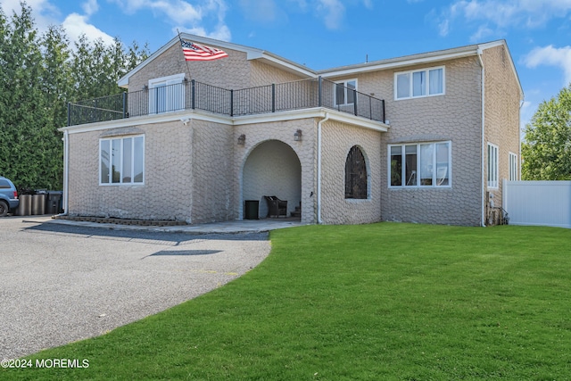 view of front facade with brick siding, a front yard, a patio area, fence, and a balcony