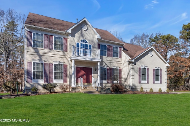 georgian-style home featuring a balcony, a front lawn, and stucco siding