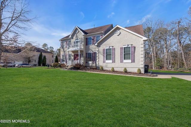 view of front of house with a balcony, stucco siding, and a front yard