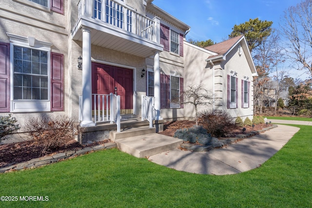 property entrance with a yard, a balcony, and stucco siding