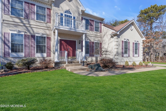 view of front facade featuring a balcony, a front lawn, and stucco siding